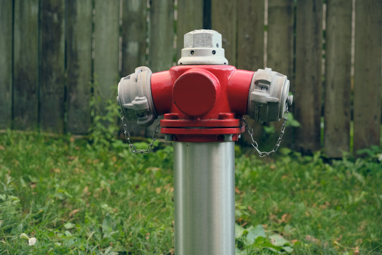 A vibrant red fire hydrant standing on green grass with wooden fence backdrop in Riga, Latvia.